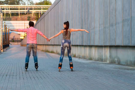 Couple on rollerblades holding hands. Back view of inline skaters. Be free like birds.の写真素材