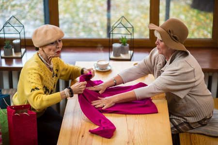Two senior women with clothes. Ladies sitting at cafe table. Quality of fabric is perfect.の写真素材