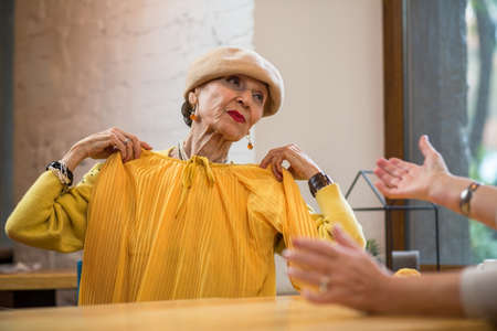 Senior woman holding clothes. Old lady indoors. Bright colors suit me.の写真素材