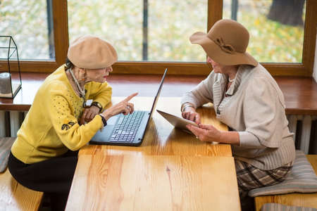 Two senior women and laptop. Old ladies with tablet. Comparison of gadgets.の写真素材