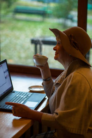 Elderly woman with a laptop. Senior woman holding coffee cup. Morning of modern citizen.