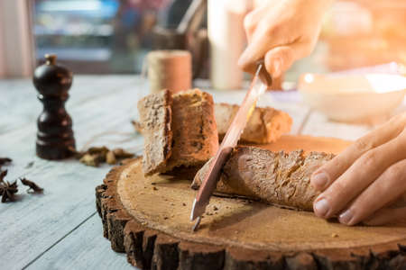 Hands with knife cutting baguette. Bread on wooden board. Baked products of finest quality.の写真素材