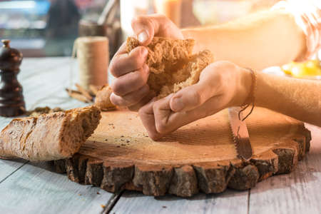 Hands breaking bread. Baguette piece on wooden board. Finest baked products.の写真素材
