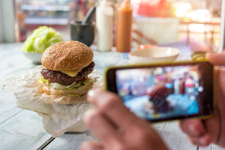 Burger on the table. Hands with phone photographing food. Share impressions about new cafe.の写真素材