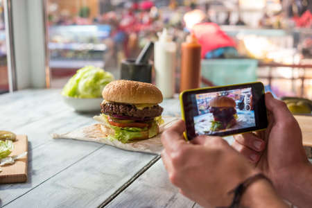 Photographing burger with cell phone. Hamburger on gray wooden table.の写真素材