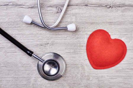 Stethoscope and red heart. Medical device on wooden backdrop. Blood pressure control.