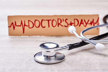 Stethoscope and greeting for doctor. Paper card on wooden backdrop. Congratulations for cardiologist.の写真素材