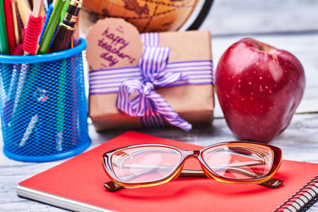 Basket with stationery and glasses. Apple, notebook and present box. Sincere wishes to teacher.の写真素材