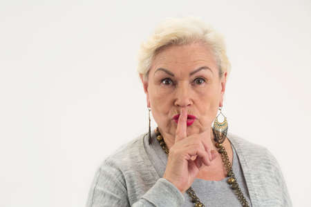 Senior lady showing silence gesture. Woman holding finger on lips. Can you keep a secret.の写真素材