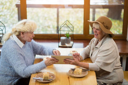 Senior women holding tablet. Cake and coffee on table. New os is much better.の写真素材