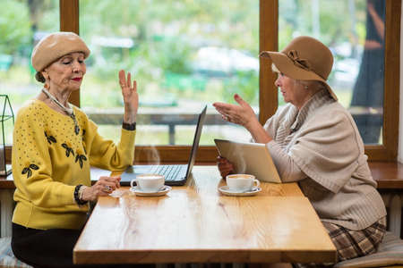 Women with gadgets in cafe. Coffee cups, laptop and tablet. Pros and cons of internet.の写真素材