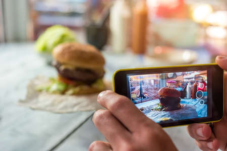 Cell phone photographing a burger. Hamburger on cafe table. The highest resolution.の写真素材