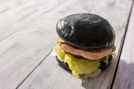 Black burger on wooden background. Meat and lettuce leaves. Unique hamburger recipe.の写真素材