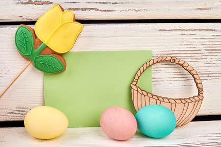 Cookie on stick, blank card. Three painted eggs, wooden surface. Spring religious holiday.