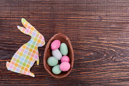 Paper rabbit cutout and sweets. Candies on brown wooden background. Sweet taste of Easter holiday.