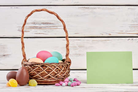 Easter basket and blank paper. Sweets on white wood.