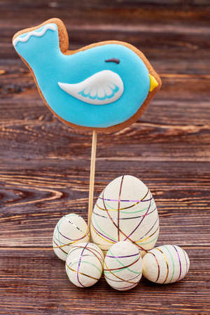 Bird cookie and Easter eggs. Glazed biscuit on wooden background.