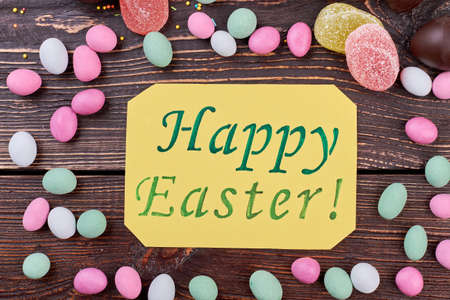 Happy Easter card with sweets. Colorful candies on dark wood.