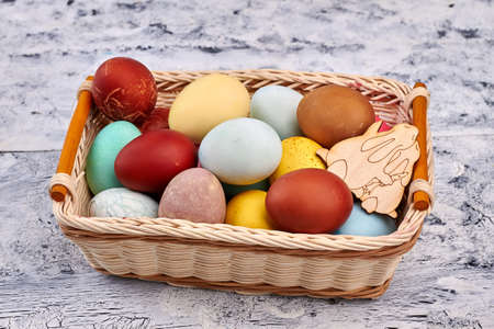 Basket with colored Easter eggs. Wicker basket, painted wood background.の写真素材