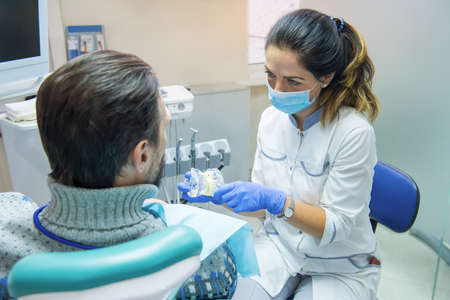 Dentist holding artificial teeth. Stomatologist with her patient. Benefits of tooth implants.
