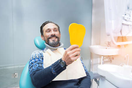 Man in dental chair. Person holding mirror and smiling. Fix your smile.の写真素材