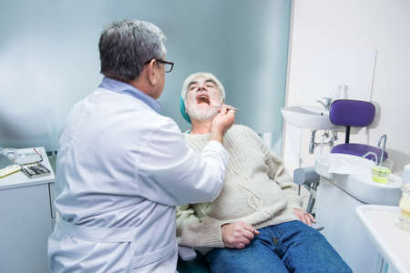 Elderly man at the stomatologist. Dentist with probe examining patient.の写真素材
