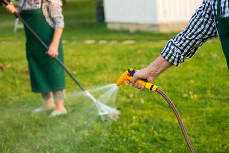 Senior hand holding water hose. Garden hose sprayer. Lawn care tips.の写真素材