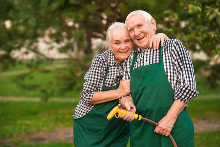 Couple of gardeners, water hose. Senior man and woman smiling. Spring gardening tips.の写真素材