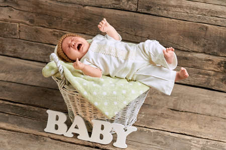 Basket with crying baby. Small child on wooden background. Loud voice of new generation.の写真素材