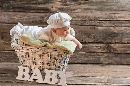 Basket and baby, wooden background. Little child lying on towel.の写真素材
