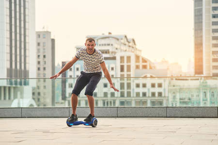 Guy riding hoverboard, city background. Young man on gyroscooter. Make friends with technology.