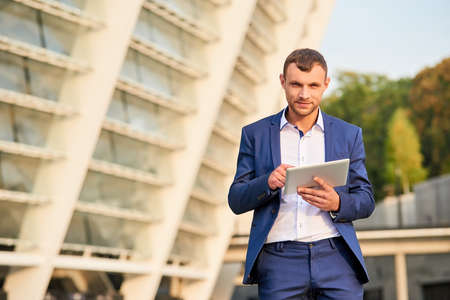 Young caucasian businessman holding tablet. Male wearing suit outdoors. Business and media.の写真素材