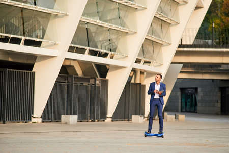 Businessman riding hoverboard. Guy with a tablet outdoors.の写真素材