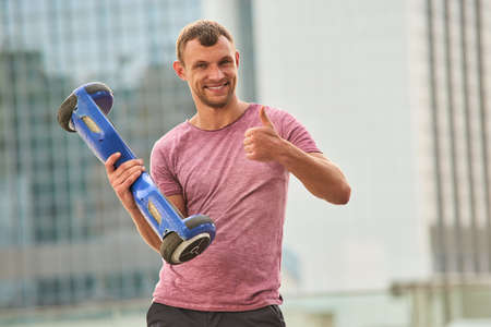 Man holding gyroboard, thumb up. Happy guy with gadget outdoors. Best hoverboard reviews.の写真素材