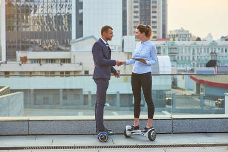 Businessman and woman shaking hands. People on hoverboards, city background. Building work relationships.の写真素材