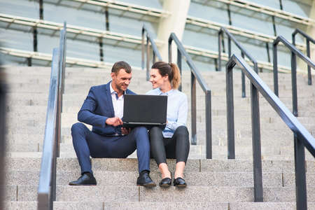 Business couple with laptop. Smiling people sitting on stairs.の写真素材