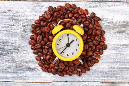 Heap of coffee beans. Alarm clock on wooden background.の写真素材