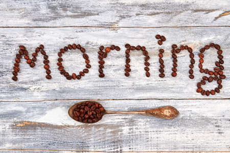 Old rusty spoon on wooden surface. Inscription morning from coffee grains.の写真素材