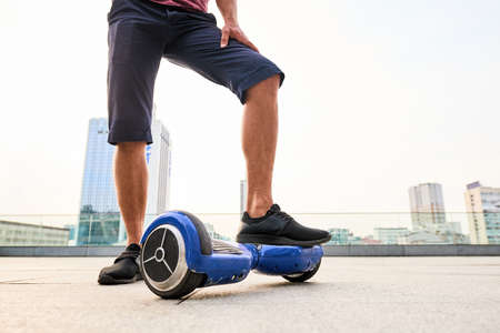 Male legs and gyroboard. Blue hoverboard on city background. Fashion and technologies.