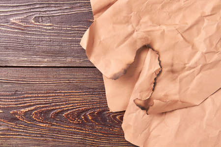 Burnt piece of vintage paper. Burned edge of torn paper, wooden background.の写真素材