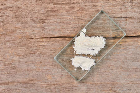 Concept of drugs addiction. White powder on glass, wooden background.の写真素材
