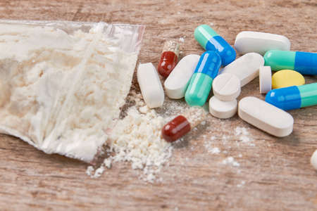 Narcotics use kills the health. White powder, pills, wooden background close up.の写真素材