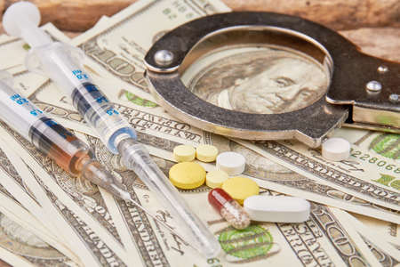 Punishment of narcotics traders. Amount of dollars, pills, syringes, handcuffs.の写真素材