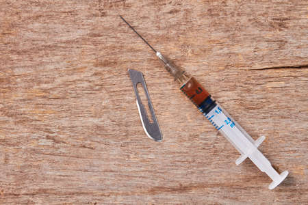 The truth about drugs. Syringe with substance, blade, old wooden background.