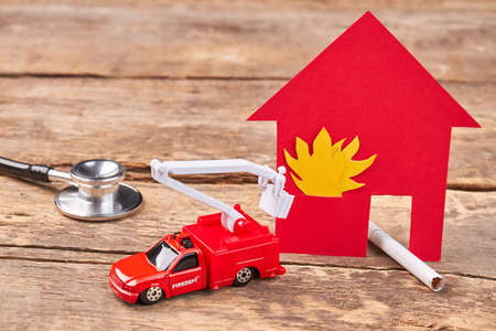 Burn cigarette caused the fire. Stethoscope, toy flaming building, toy fire truck, cigarette, wooden background. Do not play with fire.の写真素材