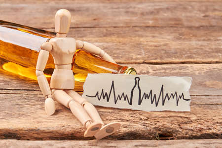 Human wooden figurine, alcohol beverage. Wooden dummy, image of heart beat, wooden background.