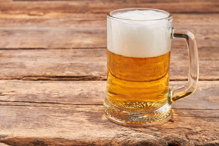 Glass mug with beer and foam. Full transparent glass of beer on old wooden background.の写真素材