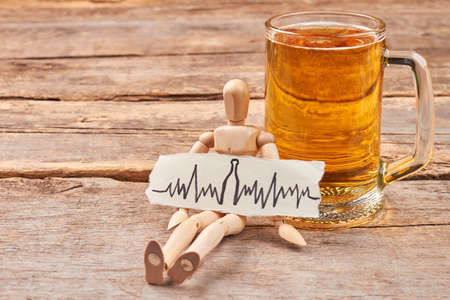 Abuse of beer leads to heart disease. Heartbeat image, human wooden dummy, mug with beer, wooden...