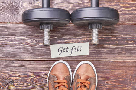 Get fit with physical exercises. Dumbbells, message, sport shoes, wooden background.の写真素材