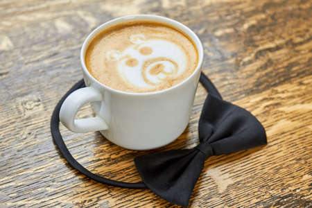 Coffee cup and bow tie. Latte on wooden background.